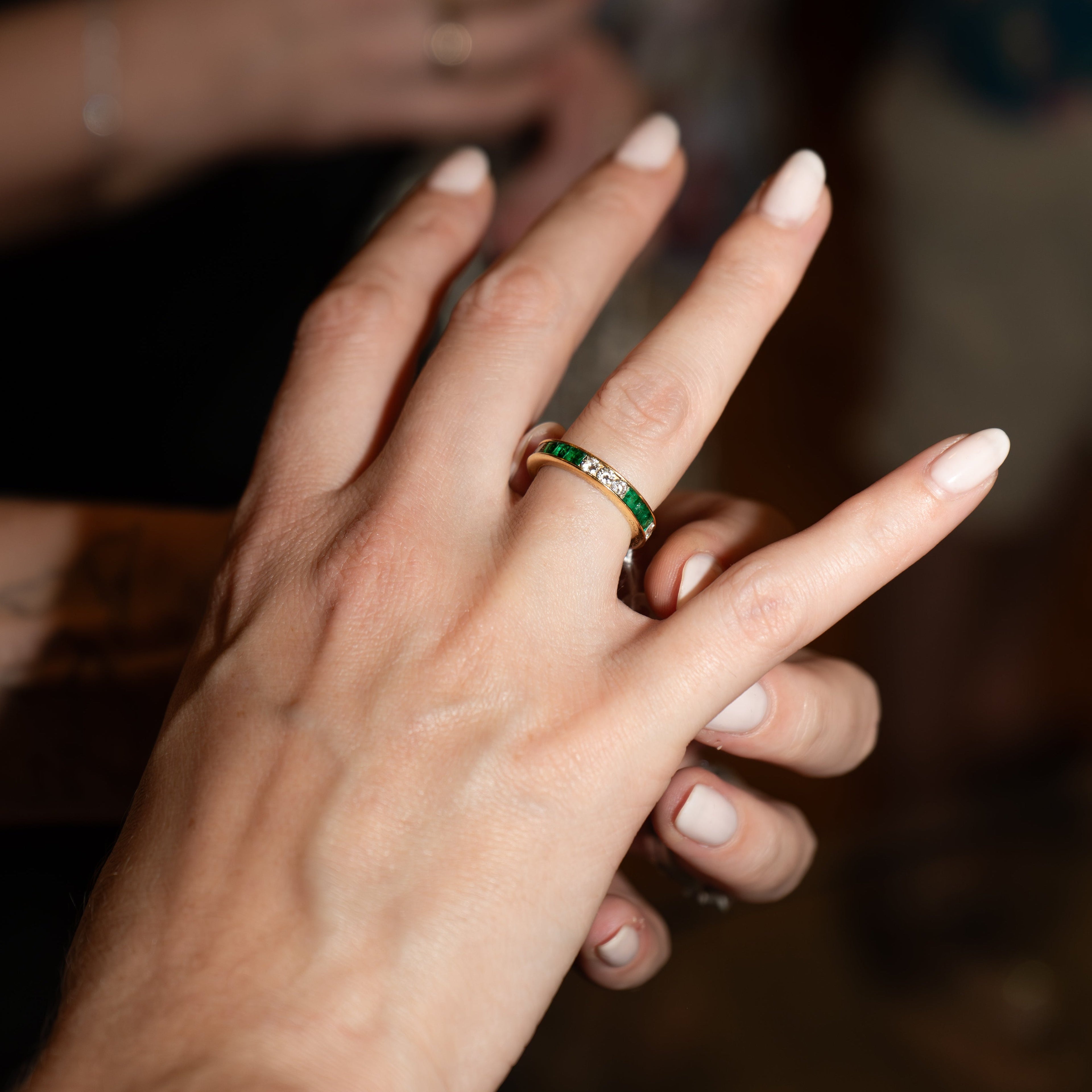 Person adjusting an emerald and diamond ring on their hand. 