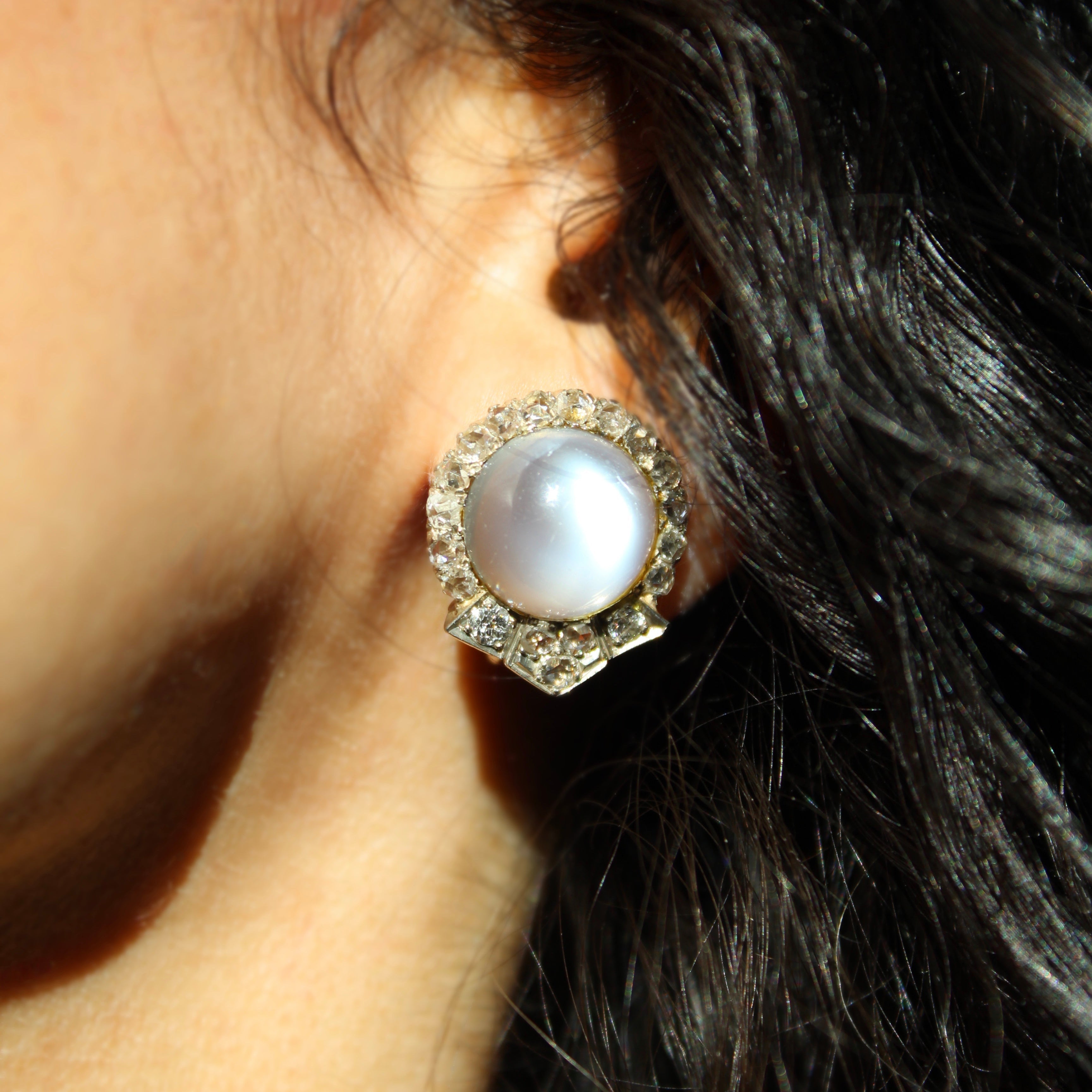 Close-up of an earring with a moonlight center worn by a person.