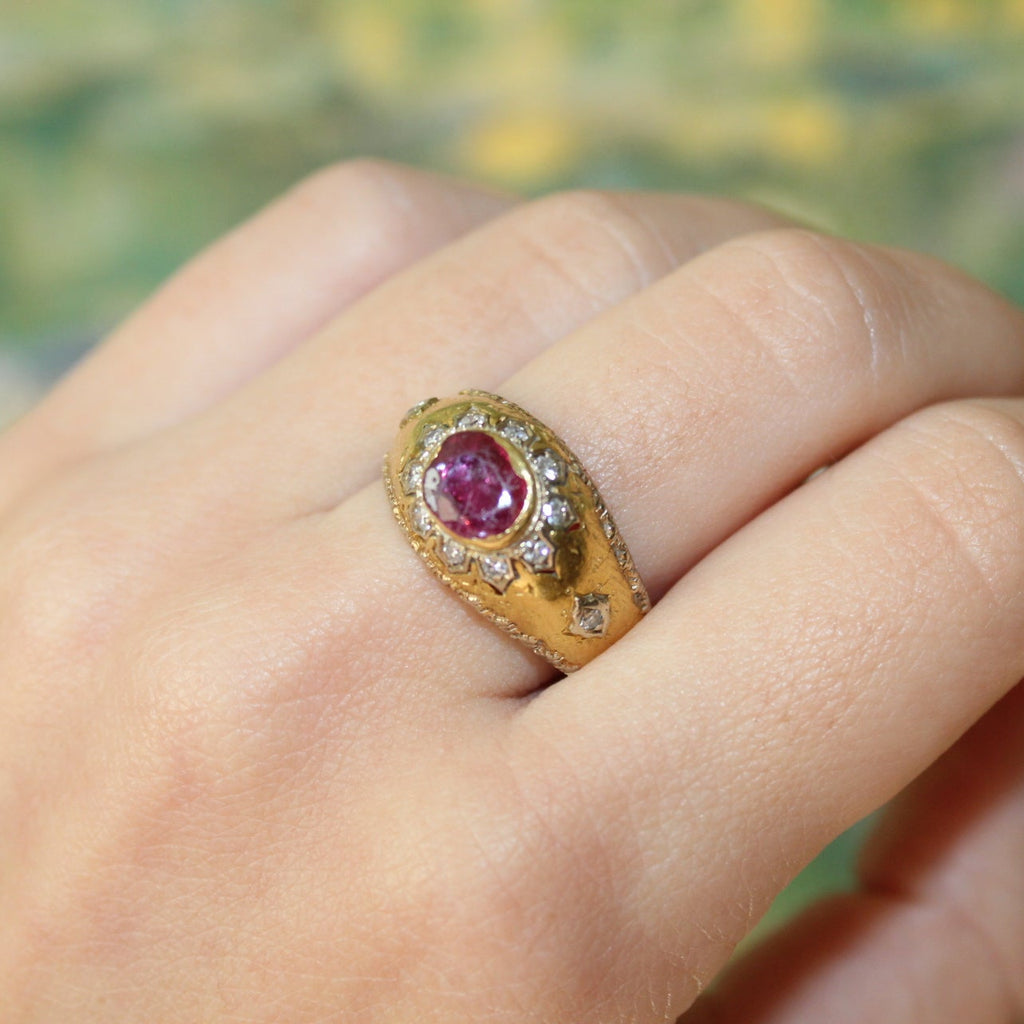 Gold ring with a ruby on a person's finger against a blurred natural background