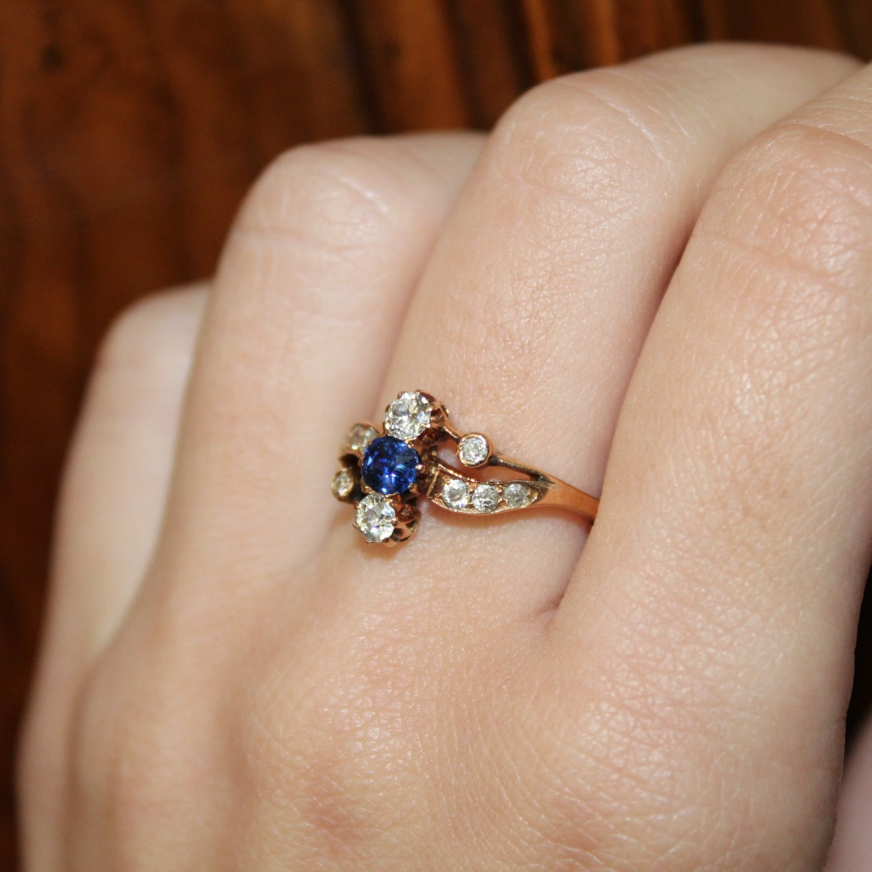 Close-up of a hand wearing a decorative ring with a blue gemstone on a wooden surface.