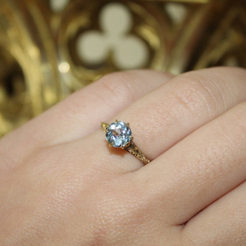 Gold ring with a blue gemstone on a hand against a gold decorative background