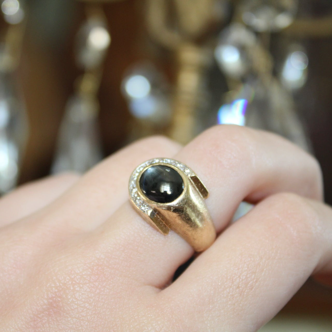 Gold ring with a black gemstone on a hand, blurred background