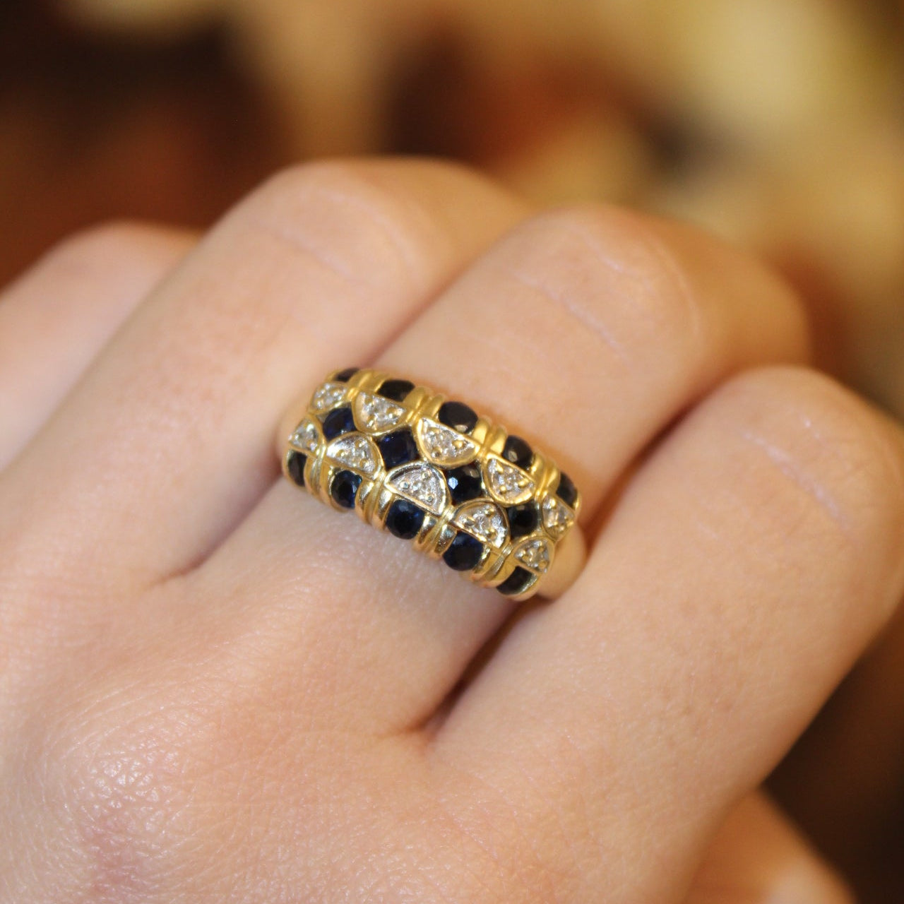 Gold and black diamond ring on a finger with a blurred background