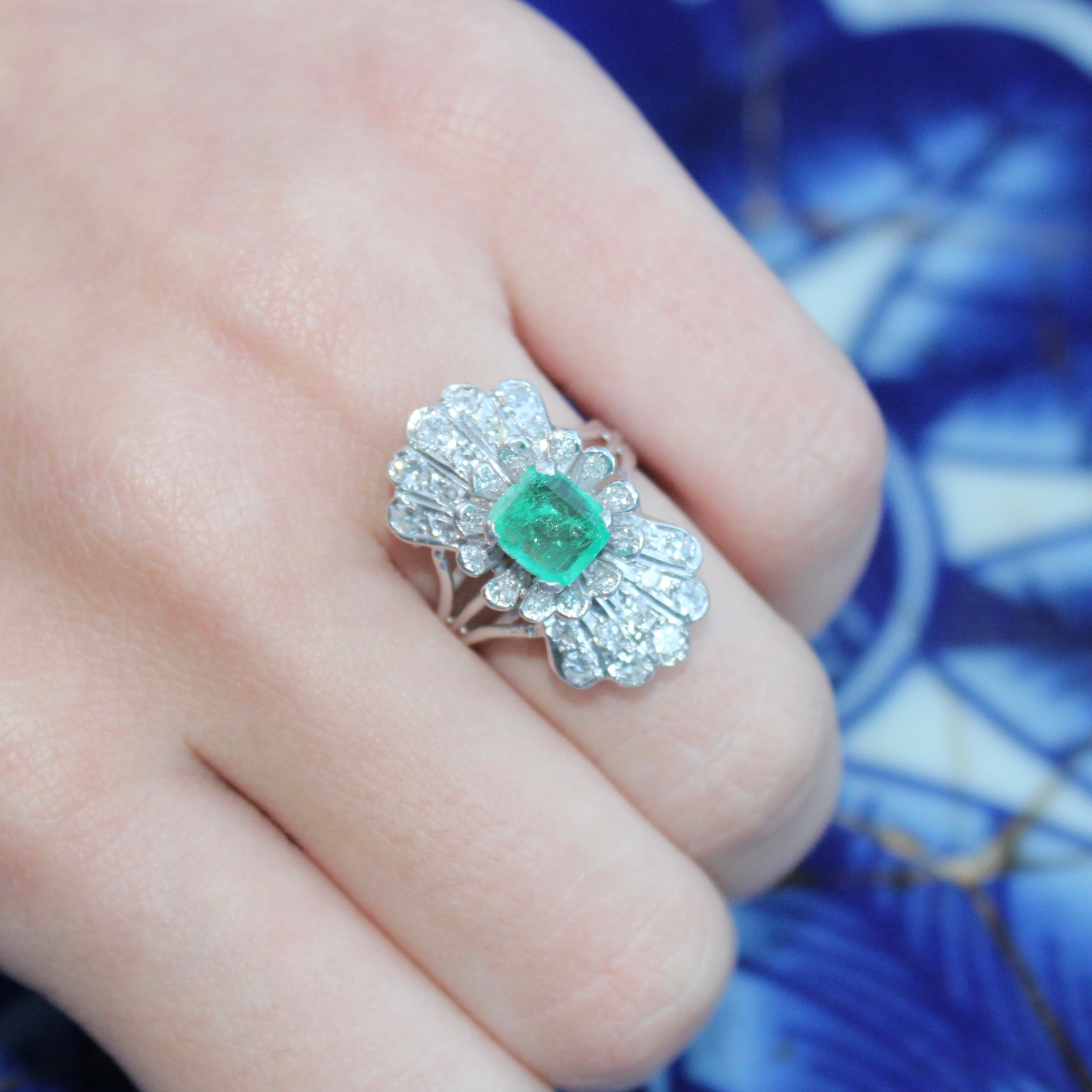 Hand wearing a decorative ring with an emerald on a blue patterned background