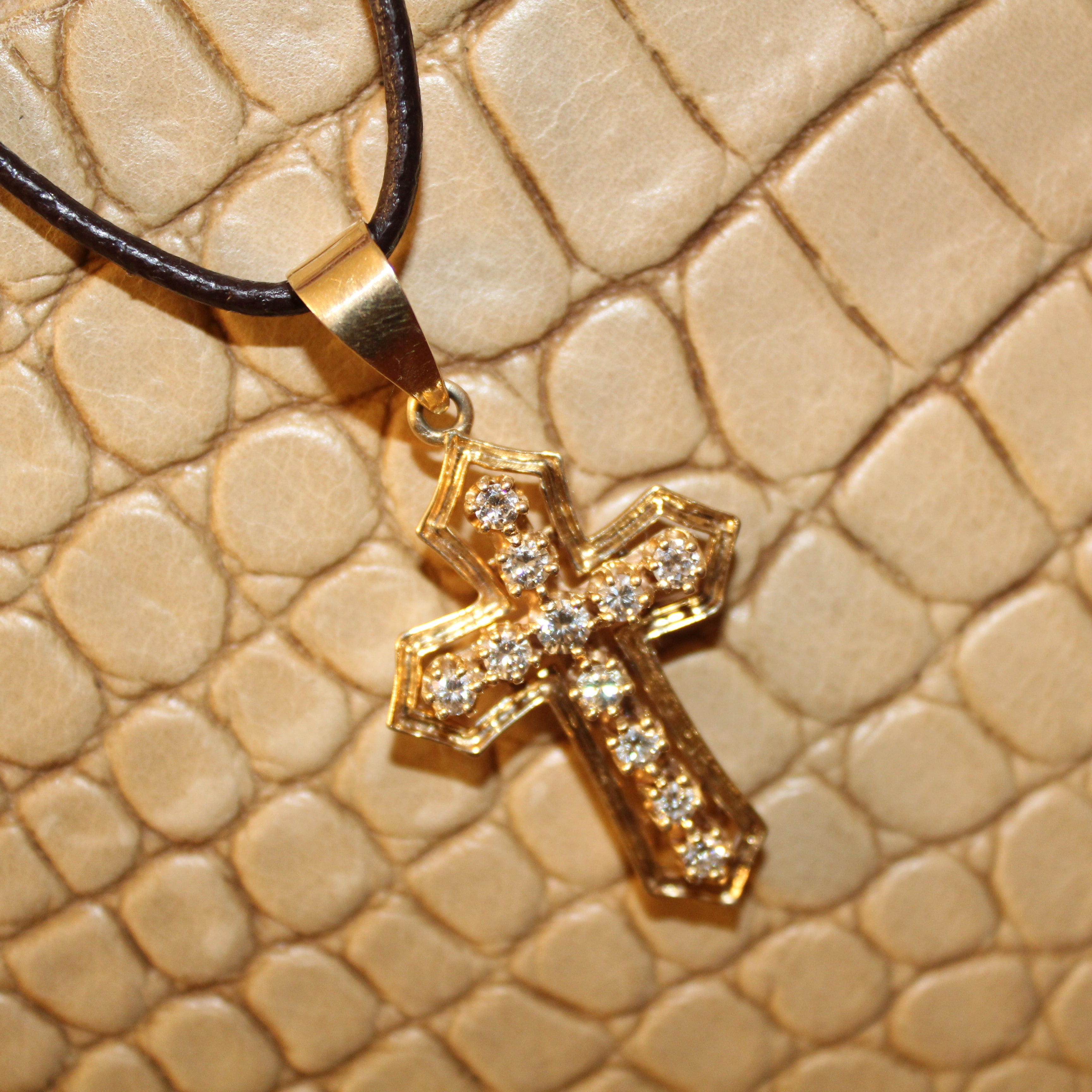 Gold cross pendant on a black cord against a beige textured background