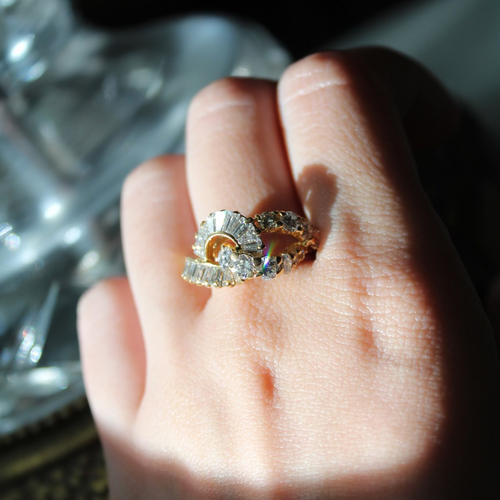 Hand wearing a gold ring with a diamond on a blurred background