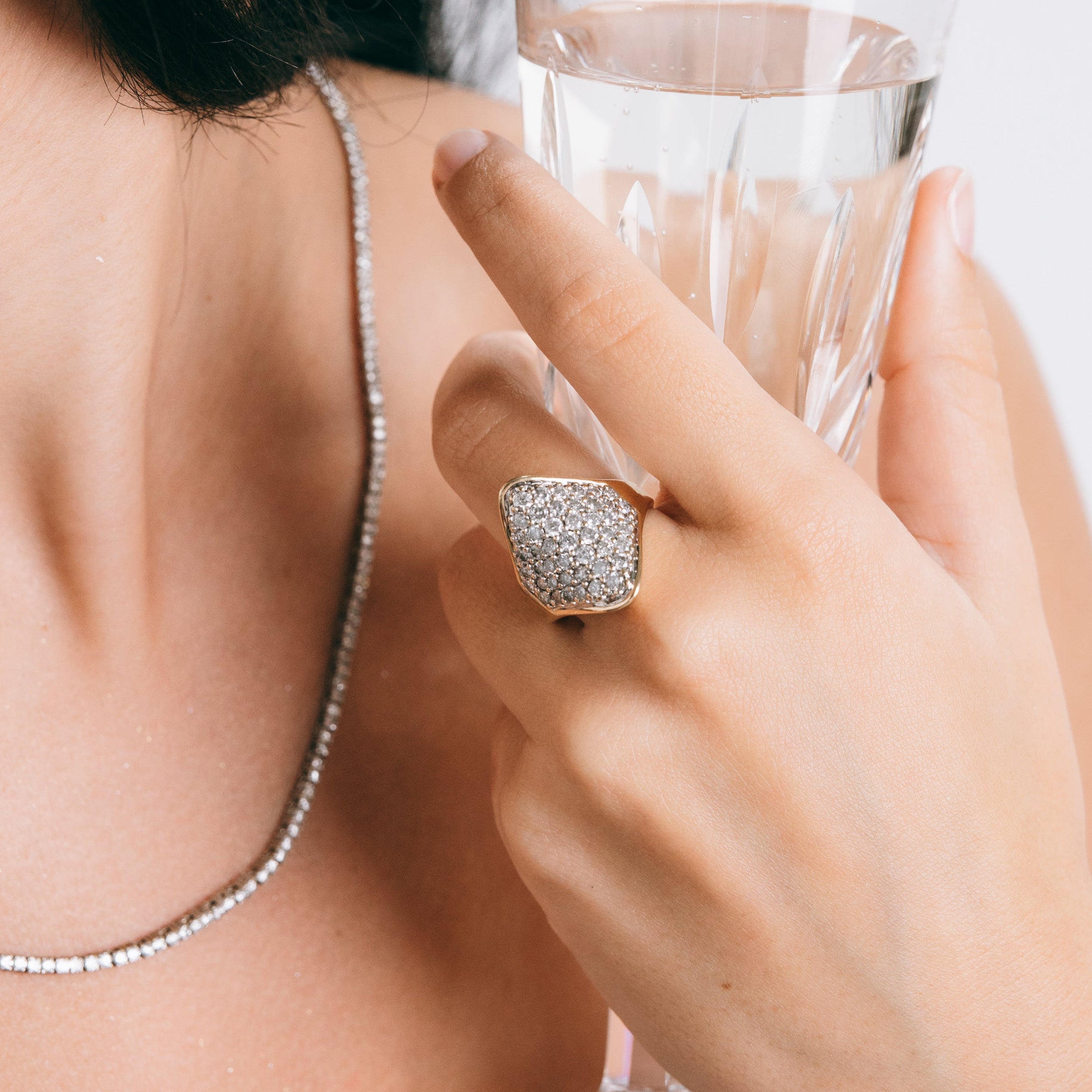 Person holding a glass of water with a diamond ring on a plain background