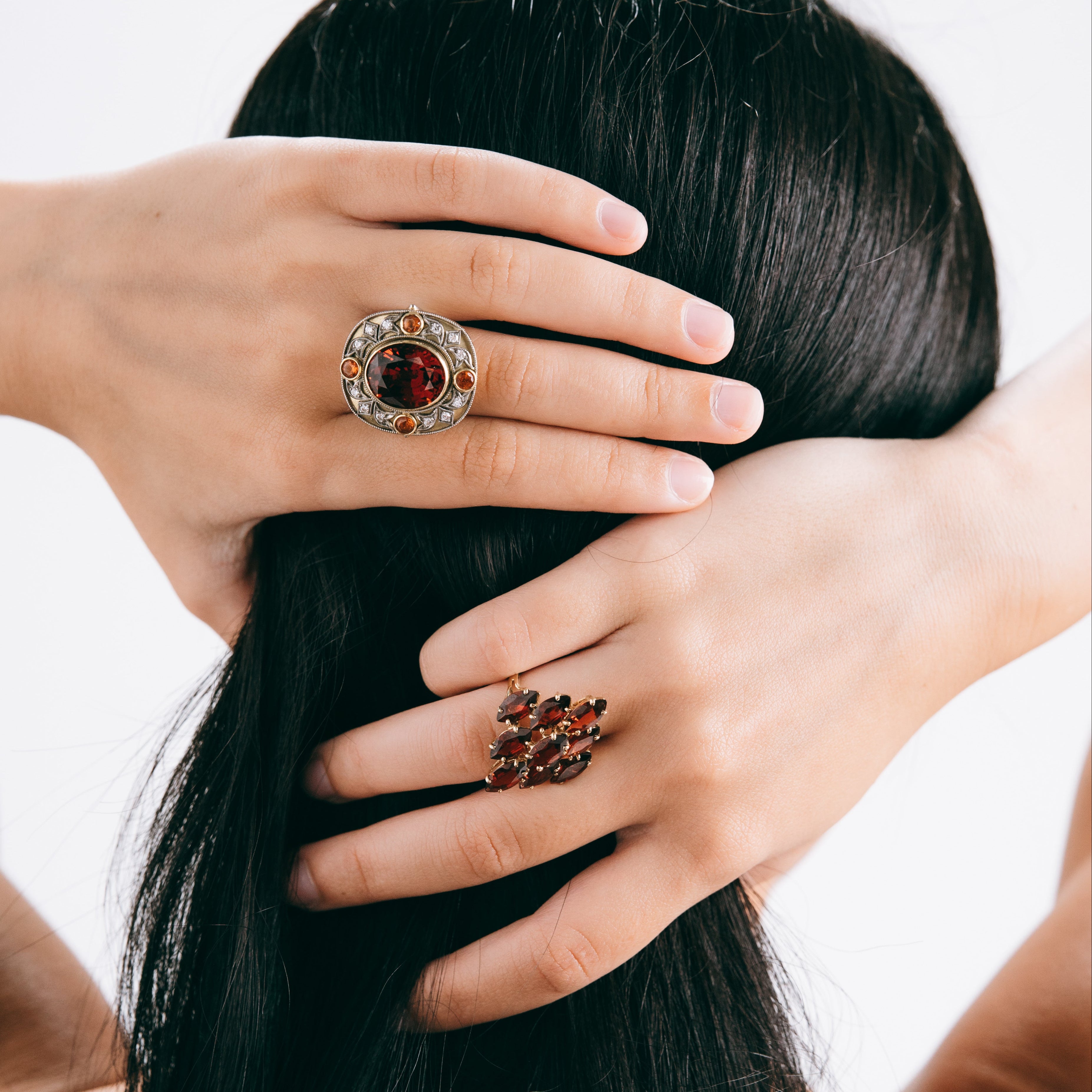 Person wearing two rings with red gemstones on a plain background