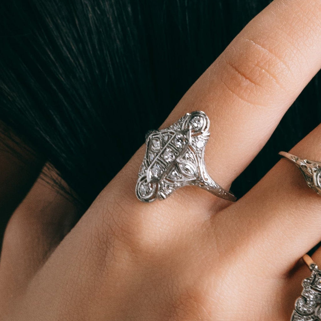 Silver ring with intricate design on a finger against a dark background