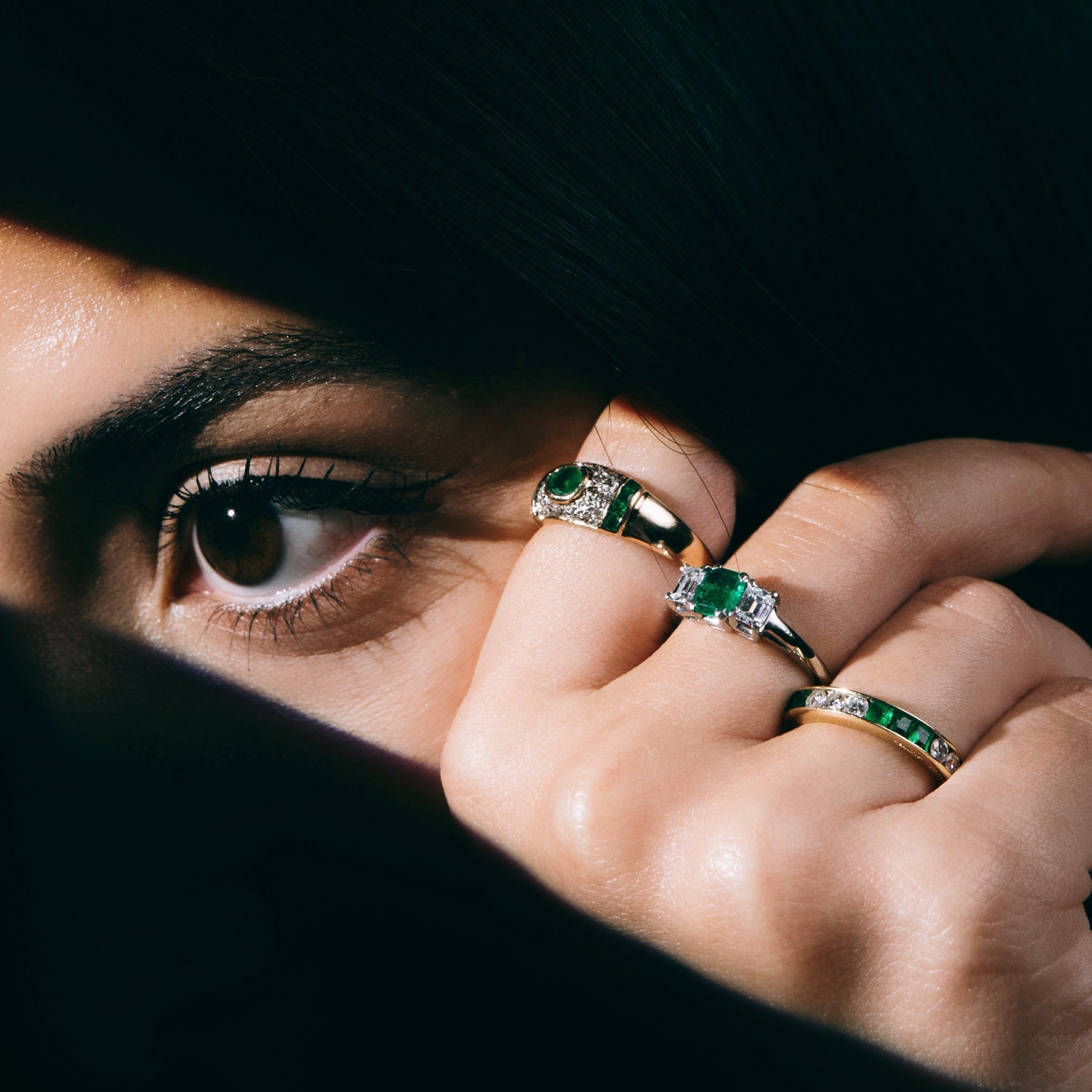 Close-up of a person wearing multiple rings with emeralds.